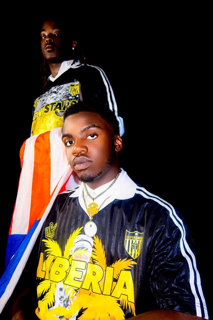 Two models wearing black-and-gold SuperSmartLIB Liberian Flag Day jerseys with a Liberian flag